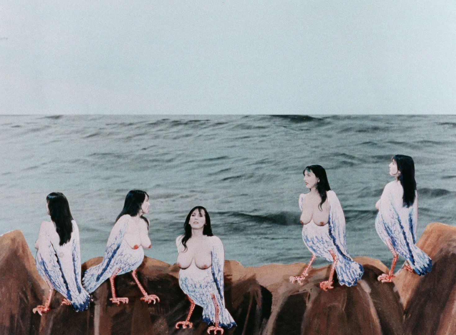 Collage image. Blue sky. Choppy ocean. Rocks in the foreground with five bird-women starring out to the sea, one starring forward. Their have large breasts and blue hair. 